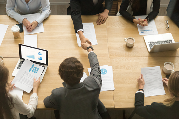 Business meeting with professionals shaking hands over a table with charts and laptops.